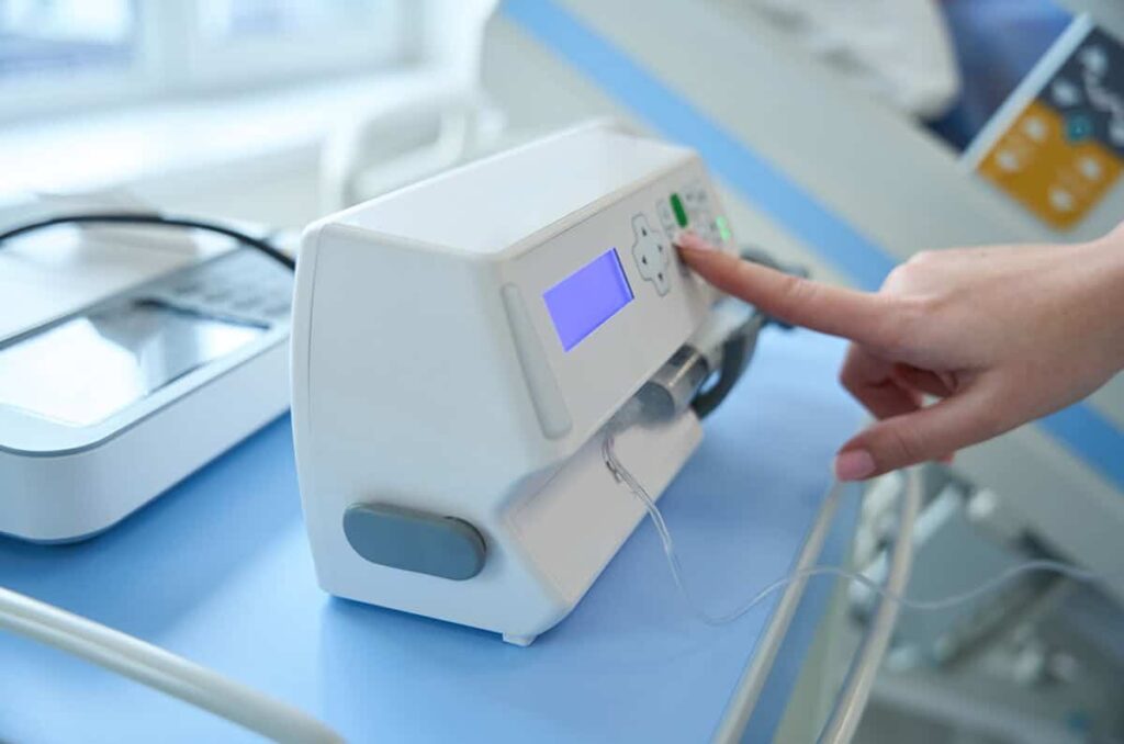 Close up of doctor hand adjusting syringe pump for anesthesia and drug administration during medical procedures in the intensive care unit