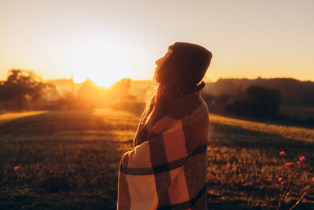 Woman wrapped in a plaid blanket facing the morning sun, representing hope while exploring PTSD treatment options