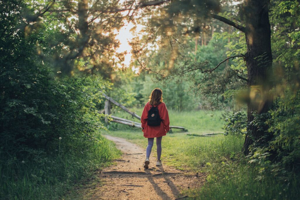 Woman with a backpack walking along a sunlit forest path, representing exploring OCD treatment options